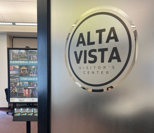 Frosted glass door with "Altavista Visitor's Center" logo on front, ajar and leading to a room with a Campbell County promotional sign inside.